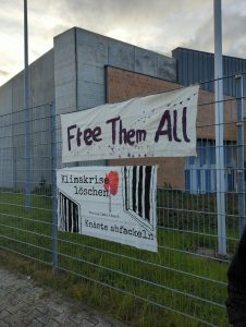 Transparent "Free Them All" und "Klimakrise löschen - Knäste abfackeln" an Zaun von JVA Luckau-Duben